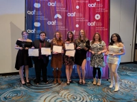 A group of art students standing in front of a backdrop with the AAF logo, holding their awards for their creative work. Art Students Earn Addy Awards for Creative Work